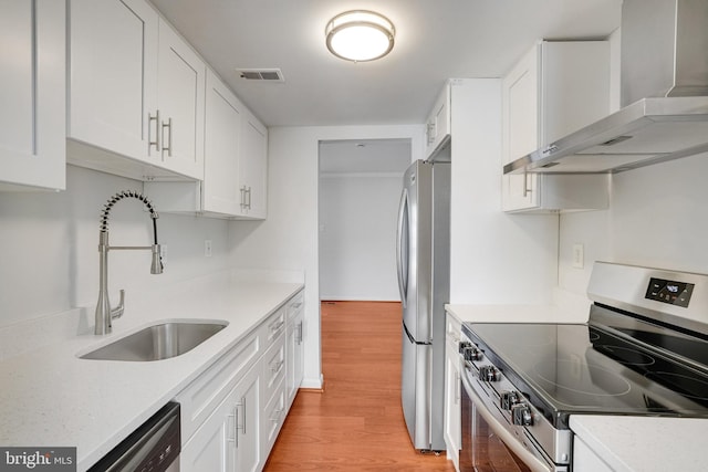 kitchen with light wood finished floors, white cabinets, stainless steel appliances, wall chimney range hood, and a sink