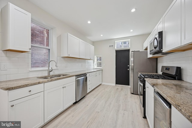 kitchen featuring stainless steel appliances, light wood finished floors, a sink, and white cabinets