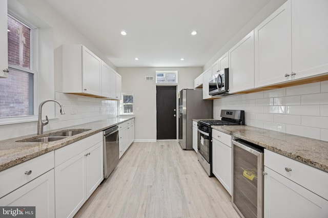 kitchen with beverage cooler, appliances with stainless steel finishes, a sink, and white cabinetry