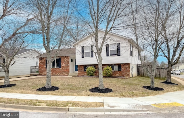 tri-level home featuring fence, a front lawn, and brick siding