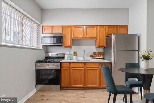 kitchen with light wood-style flooring, a sink, baseboards, light countertops, and appliances with stainless steel finishes