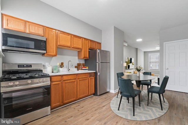 kitchen featuring stainless steel appliances, a sink, light countertops, light wood finished floors, and brown cabinetry