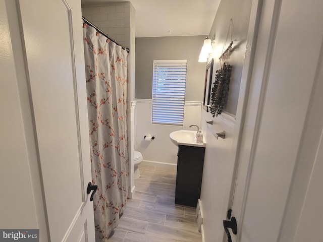 full bathroom with wood finish floors, a wainscoted wall, curtained shower, toilet, and vanity