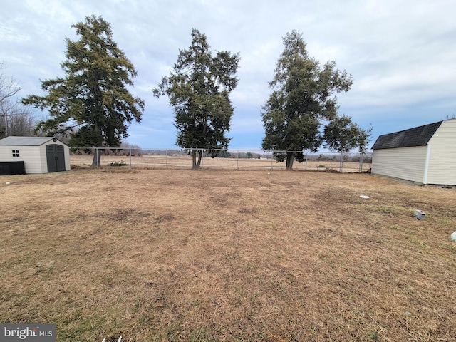 view of yard with a rural view, fence, an outdoor structure, and a shed