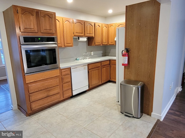 kitchen with a sink, stainless steel oven, baseboards, light countertops, and dishwasher