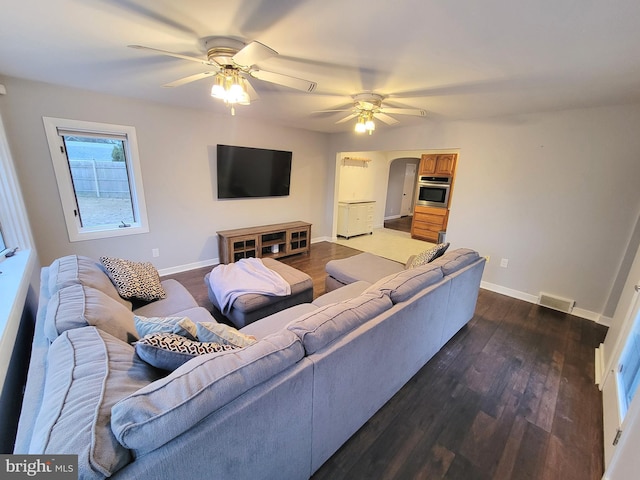 living room featuring arched walkways, ceiling fan, dark wood-style flooring, visible vents, and baseboards