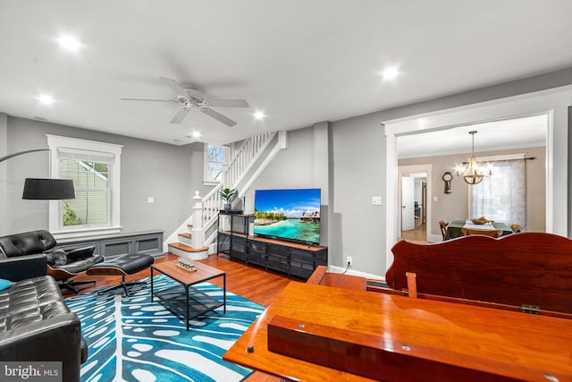 living room with recessed lighting, ceiling fan with notable chandelier, wood finished floors, stairway, and crown molding