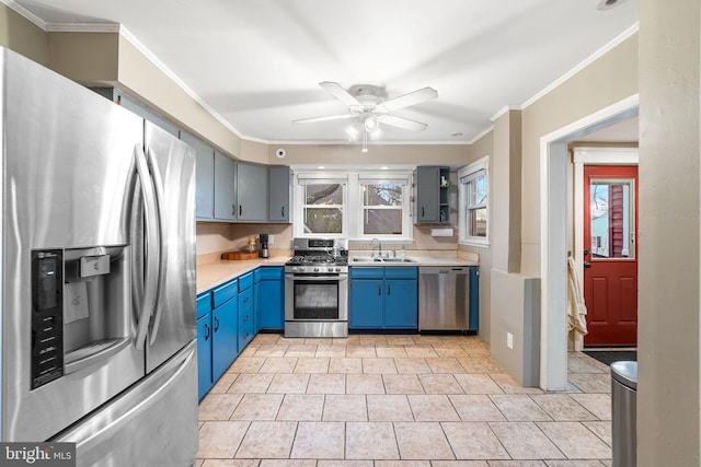 kitchen featuring a sink, light countertops, appliances with stainless steel finishes, blue cabinetry, and crown molding