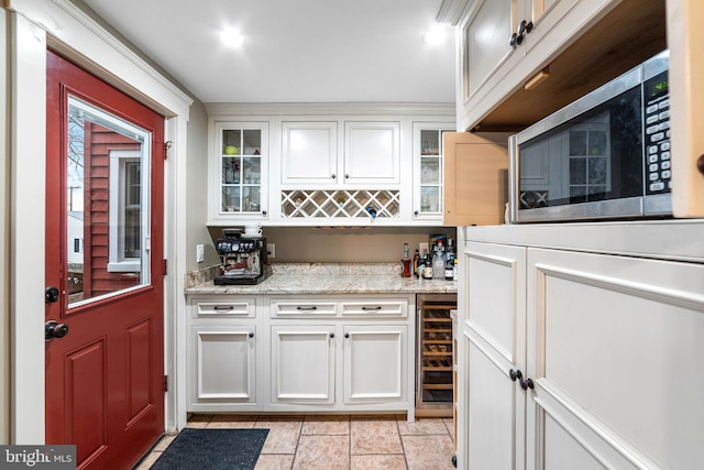 kitchen with light stone counters, stainless steel microwave, glass insert cabinets, white cabinets, and beverage cooler