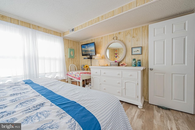 bedroom featuring crown molding, visible vents, wood walls, a textured ceiling, and light wood-type flooring