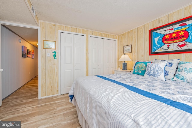 bedroom featuring ornamental molding, light wood-type flooring, a textured ceiling, and two closets