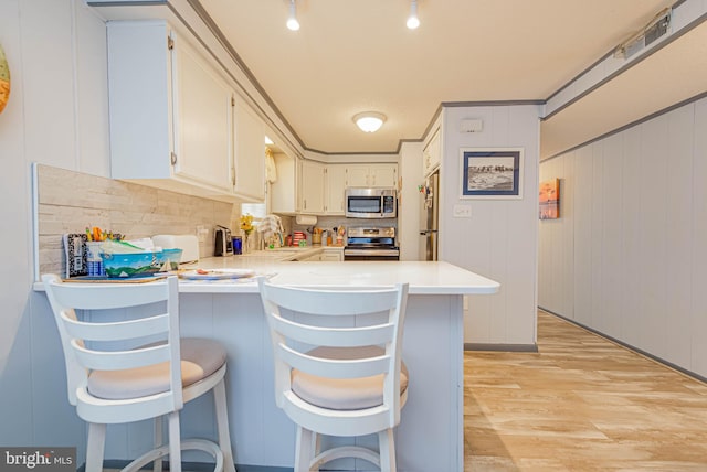 kitchen with light wood finished floors, light countertops, appliances with stainless steel finishes, and a peninsula