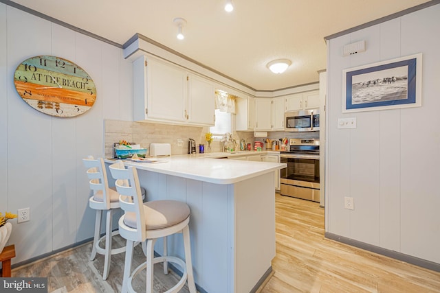 kitchen featuring a peninsula, stainless steel appliances, light countertops, light wood-style floors, and backsplash