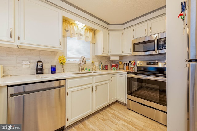 kitchen featuring stainless steel appliances, light countertops, light wood-style flooring, a sink, and a textured ceiling