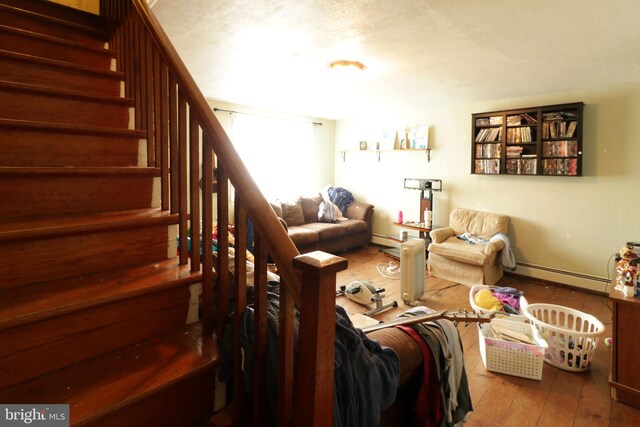 living area with hardwood / wood-style flooring, baseboard heating, and stairs