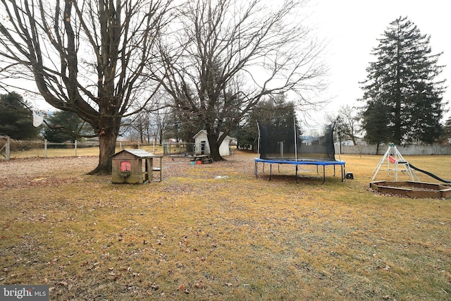 exterior space featuring an outbuilding, a playground, a storage shed, fence, and a trampoline