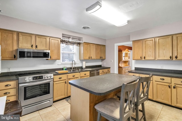 kitchen featuring appliances with stainless steel finishes, a breakfast bar area, dark countertops, and a sink