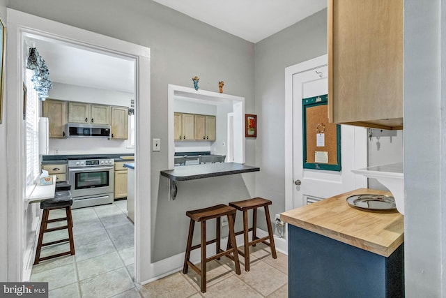 kitchen with light tile patterned flooring, baseboards, a kitchen breakfast bar, appliances with stainless steel finishes, and dark countertops