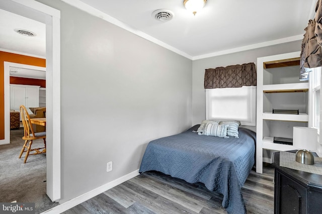 bedroom with baseboards, visible vents, crown molding, and wood finished floors