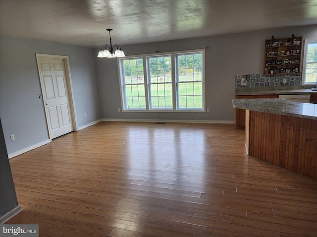 unfurnished dining area featuring a chandelier, baseboards, and hardwood / wood-style flooring