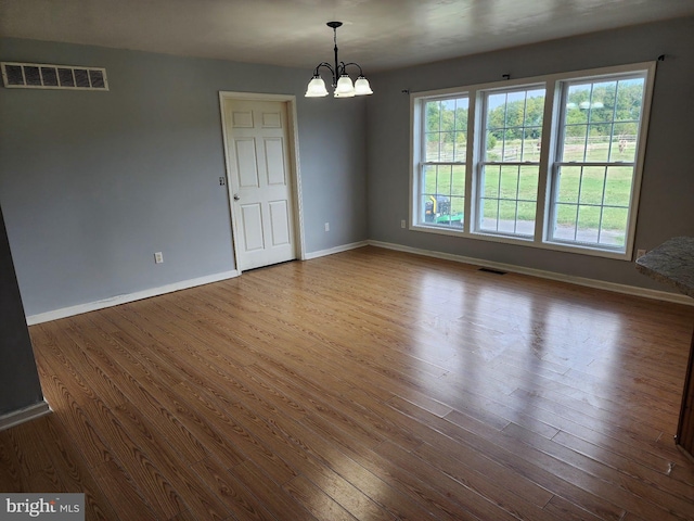 spare room featuring dark wood-style floors, baseboards, visible vents, and an inviting chandelier