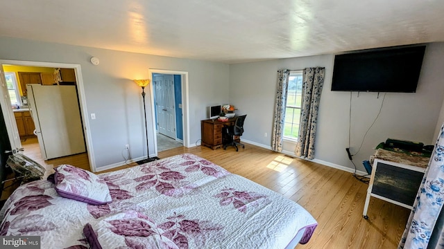 bedroom with baseboards, ensuite bathroom, freestanding refrigerator, and light wood-style floors