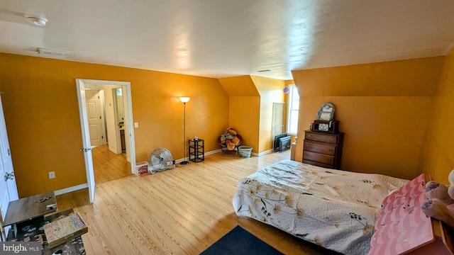 bedroom with lofted ceiling, wood finished floors, visible vents, and baseboards