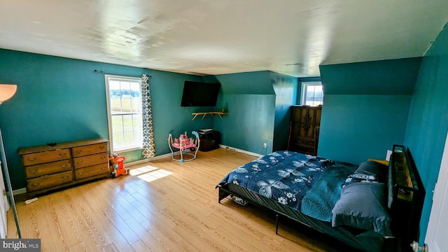 bedroom with vaulted ceiling, wood finished floors, and baseboards