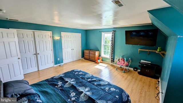 bedroom featuring wood finished floors, visible vents, baseboards, and two closets