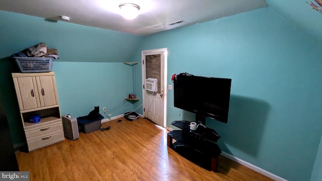 interior space featuring cooling unit, wood finished floors, visible vents, baseboards, and vaulted ceiling