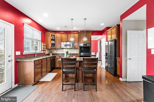 kitchen featuring stainless steel appliances, wood finished floors, a kitchen island, backsplash, and brown cabinets