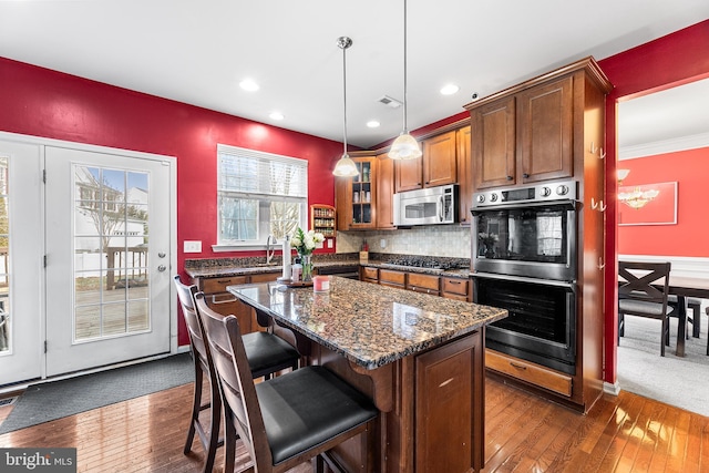 kitchen with brown cabinetry, a kitchen island, glass insert cabinets, a breakfast bar, and stainless steel appliances