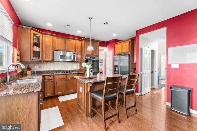 kitchen with appliances with stainless steel finishes, brown cabinetry, a sink, and a kitchen island