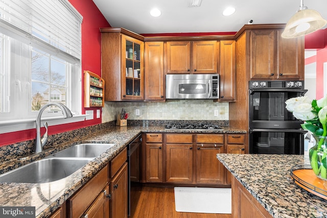 kitchen with dark stone counters, black appliances, a sink, and brown cabinets