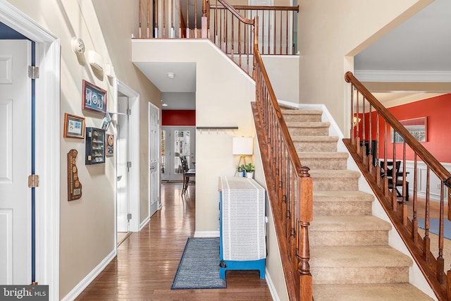 stairway featuring wood-type flooring, a high ceiling, baseboards, and ornamental molding