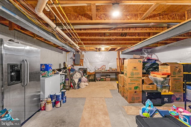 unfinished basement with electric panel and stainless steel fridge with ice dispenser