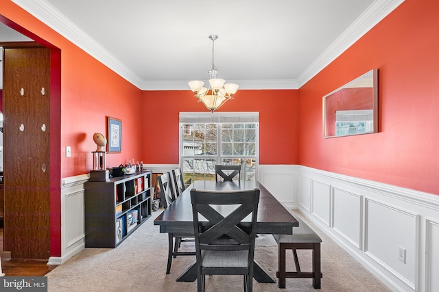 dining room featuring wainscoting, ornamental molding, an inviting chandelier, carpet, and a decorative wall