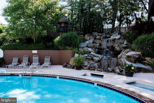 community pool with a patio area, fence, and a jacuzzi