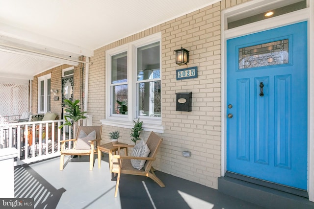 doorway to property featuring a porch and brick siding