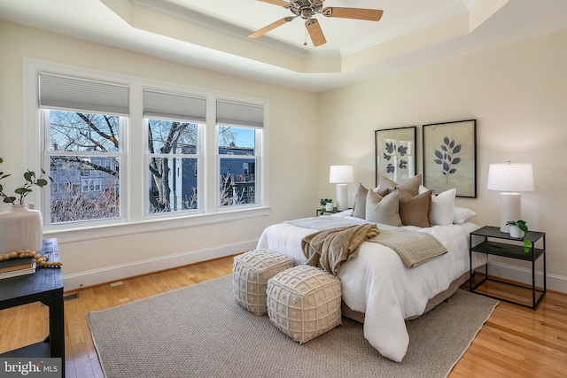 bedroom with a tray ceiling, crown molding, light wood finished floors, ceiling fan, and baseboards