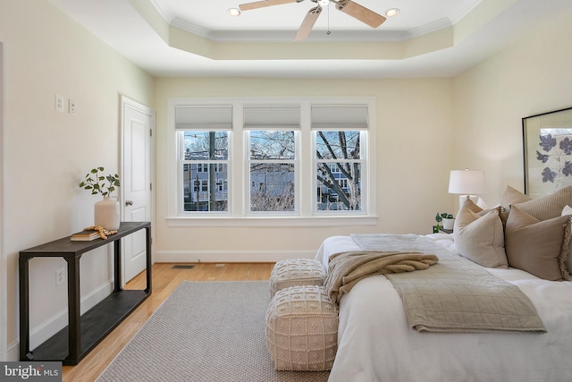 bedroom with light wood-type flooring, ornamental molding, and a raised ceiling