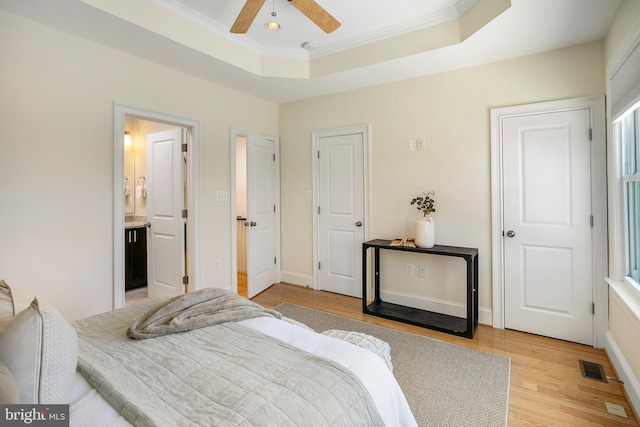 bedroom featuring a raised ceiling, visible vents, ornamental molding, ensuite bath, and light wood-type flooring