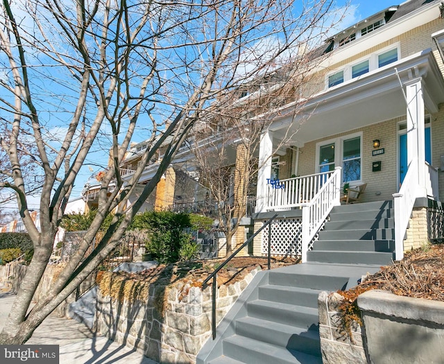 view of front of house featuring covered porch, stairs, and brick siding