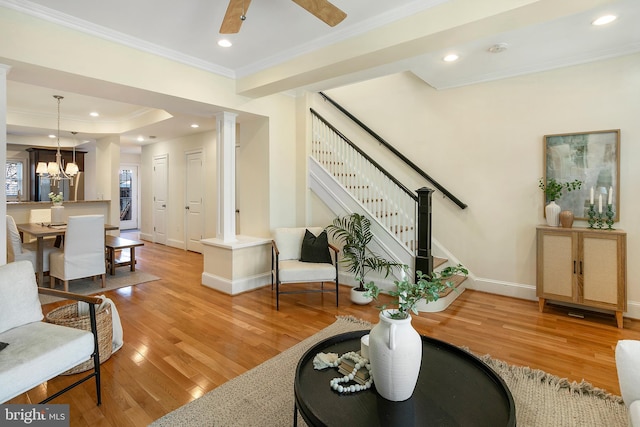 living area with baseboards, hardwood / wood-style flooring, stairway, ornamental molding, and ceiling fan with notable chandelier