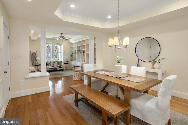 dining space featuring decorative columns, a tray ceiling, light wood-style flooring, and ornamental molding