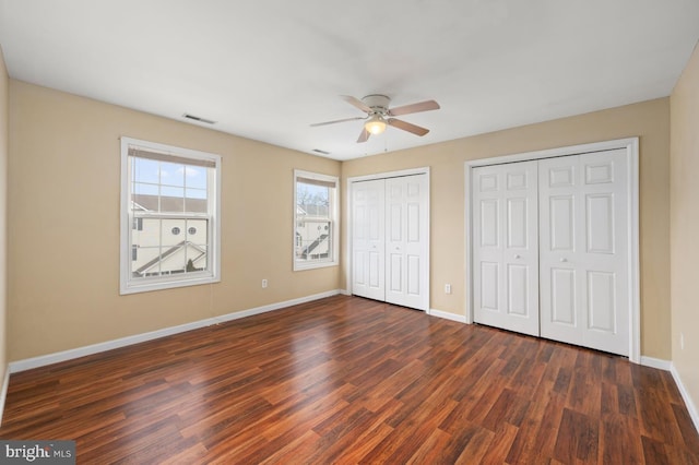 unfurnished bedroom featuring dark wood-style floors, two closets, visible vents, and baseboards