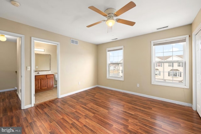 unfurnished bedroom featuring dark wood-type flooring, ensuite bath, visible vents, and baseboards