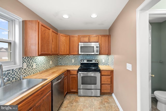 kitchen with decorative backsplash, appliances with stainless steel finishes, brown cabinetry, a sink, and baseboards