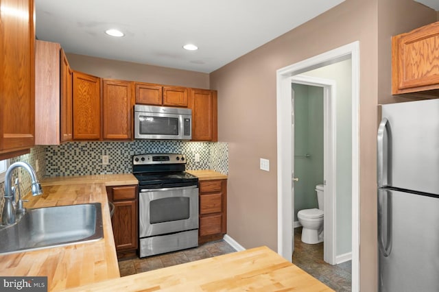 kitchen with stainless steel appliances, wooden counters, backsplash, a sink, and baseboards