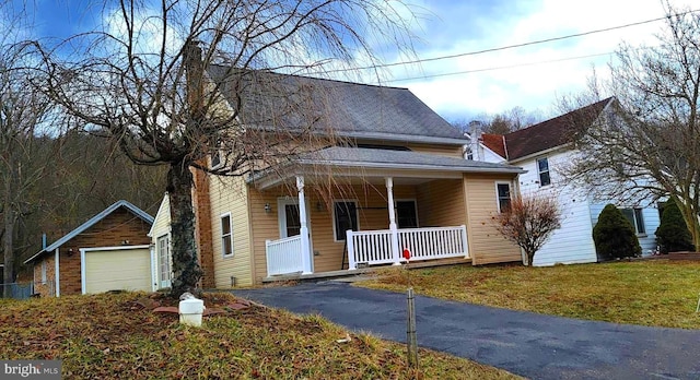 view of front of house featuring covered porch, a shingled roof, a front yard, and a garage